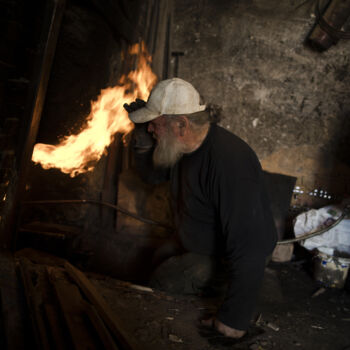 In this Friday, Nov. 20, 2017 photo, sculptor and ceramicist Haralambos Goumas looks into the fire as he tries to control the temperature of the furnace in his workshop in the Egaleo suburb of Athens. (AP Photo/Petros Giannakouris)