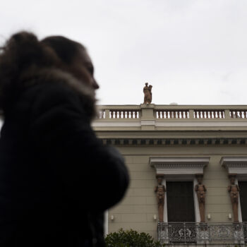 In this Thursday, Dec. 21, 2017 photo, a woman walks past a neoclassical building decorated with terracotta statues of the muses, on the roof, and Atlases, flanking the windows, made by sculptor and ceramicist Haralambos Goumas in Piraeus, the port of Athens. (AP Photo/Petros Giannakouris)
