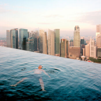 A man floats in the 57th-floor swimming pool of the Marina Bay Sands Hotel, with the skyline of “Central,” the Singapore financial district, behind him. Singapore